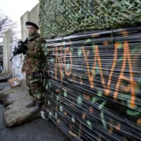 Dressed as a British Army soldier, a member of the anti-Brexit campaign group \"Border Communities Against Brexit\" poses with a wall installed on a road crossing the border between Northern Ireland and the Republic of Ireland during a demonstration in Newry, Northern Ireland, on Saturday. | AFP-JIJI