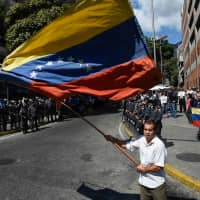 An opposition demostrator waves a Venezuelan national flag during a protest against the government of President Nicolas Maduro, called by opposition leader and self-proclaimed \"acting president\" Juan Guaido, outside \"Dr. JM de los Rios\" Children\'s Hospital in Caracas on Wednesday. | AFP-JIJI