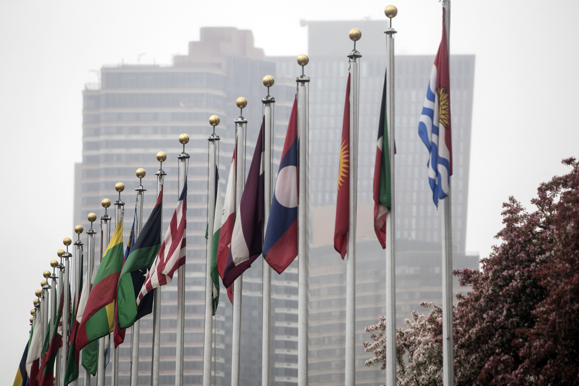 National flags fly outside the secretariat building at the United Nations headquarters in New York. | BLOOMBERG
