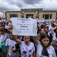 Demonstrators hold a placard reading \"Colombians, Let\'s not allow the war to polarize our country anymore\" as they gather at Bolivar square in Bogota to demonstrate against terrorism, in repudiation of the police academy rcar bombing, and in support of the victims and their relatives, on Sunday. | AFP-JIJI