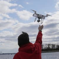 A drone operator helps to retrieve a drone after photographing over Hart Island in New York last April. Drone sightings reported by airline pilots over New Jersey renew questions about how to accommodate the popular devices into the nation\'s airspace. The ability of drones to interfere with aviation is likely to get worse as the number of machines multiplies. | AP