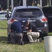 Law enforcement officials take cover outside a SunTrust Bank branch Wednesday in Sebring, Florida. Authorities say they\'ve arrested a man who fired shots inside the Florida bank. | THE NEWS SUN / VIA AP
