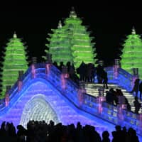 In this photo taken Friday, visitors walk over an ice bridge built next to colorful pagodas, also made from blocks of ice, at the annual Harbin International Ice and Snow festival in Harbin, a city in northeastern\'s China\'s Heilongjiang province. | AP
