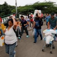 Venezuelans walk along the Simon Bolivar International Bridge as they return to their country after buying food in the Colombian border city of Cucuta on Wednesday. On Thursday, President Nicolas Maduro will be sworn in by Venezuela\'s Supreme Court, after winning a snap election last year that was boycotted by the opposition. His detractors blame him for the country\'s economic woes, which have left millions in poverty while another 2.3 million, according to the United Nations, have fled the country since 2015. | AFP-JIJI