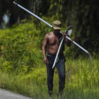 A worker, carrying tools to harvest oil palm fruit, walks along a road at a plantation in Subulussalam district in Aceh province, Indonesia, on Thursday. | AFP-JIJI