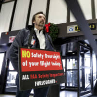 Federal Aviation Administration employee Michael Jessie, who is currently working without pay as an aviation safety inspector for the New York international field office overseeing foreign air carriers, holds a sign while attending a news conference at Newark Liberty International Airport Tuesday in Newark, New Jersey. U.S. Sens. Cory Booker and Bob Menendez called a news conference at the airport to address the partial government shutdown, which is keeping some airport employees working without pay. | AP