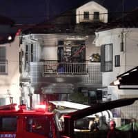 Firefighters investigate a home where a fire broke out in the early hours of Sunday in Hino, Tokyo. | KYODO