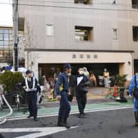 Police officers and firefighters are seen Friday in front of a lodging house in Yokohama where a fire broke out earlier in the day, killing two people. | KYODO