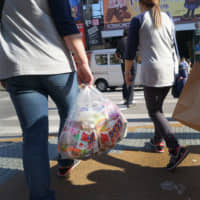 Tourists carry shopping bag from Daikoku Co. Daikoku Drug Store in Naha, Okinawa Prefecture, last March.  | Bloomberg
