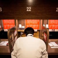 A customer in a partitioned booth eats ramen at a restaurant in Tokyo in 2018. | AFP-JIJI
