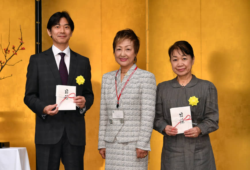Hideki Asahi, executive sales officer and manager of the media enterprise department at The Japan Times (left), and Toshiko Hasegawa, president of the Japan National Student Association Fund (right), pose for a photo with Ikebana International Tokyo Founding Chapter President Misako Ishii.