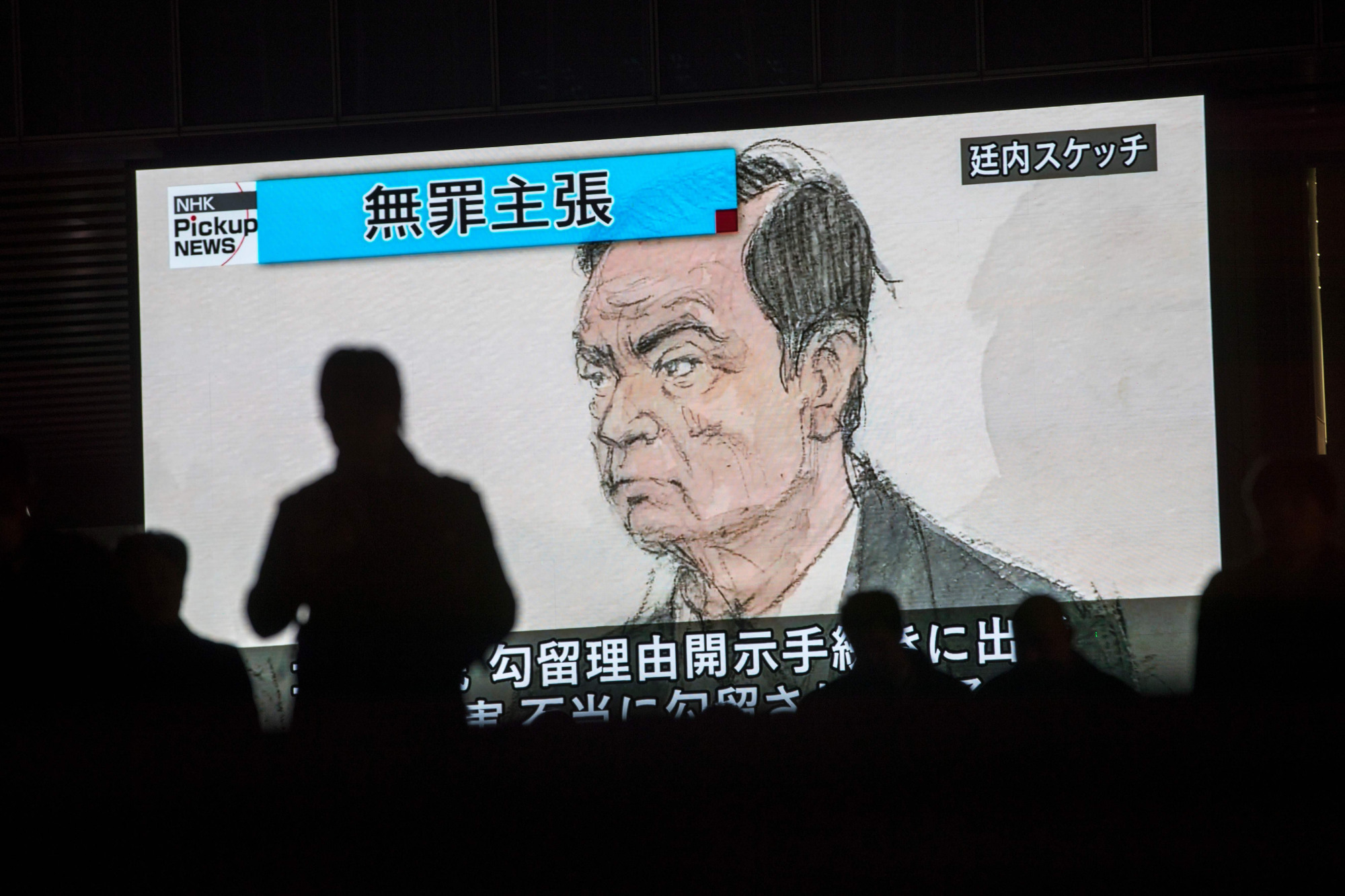 Pedestrians pass a screen showing a news program displaying a sketch of former Nissan chief Carlos Ghosn in the Tokyo District Court on Wednesday. The court rejected an appeal by Ghosn's lawyers for his release from detention, where he has been held since Nov. 19. | AFP-JIJI