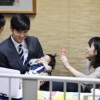 Shohei Ohtani (center) holds one-year-old Shohei Kawasaki at an Osaka Prefecture hospital on Saturday. Kawasaki\'s parents, who named him after the Los Angeles Angels star, are calling for donations in order to cover the cost of his heart transplant in the United States. | KYODO
