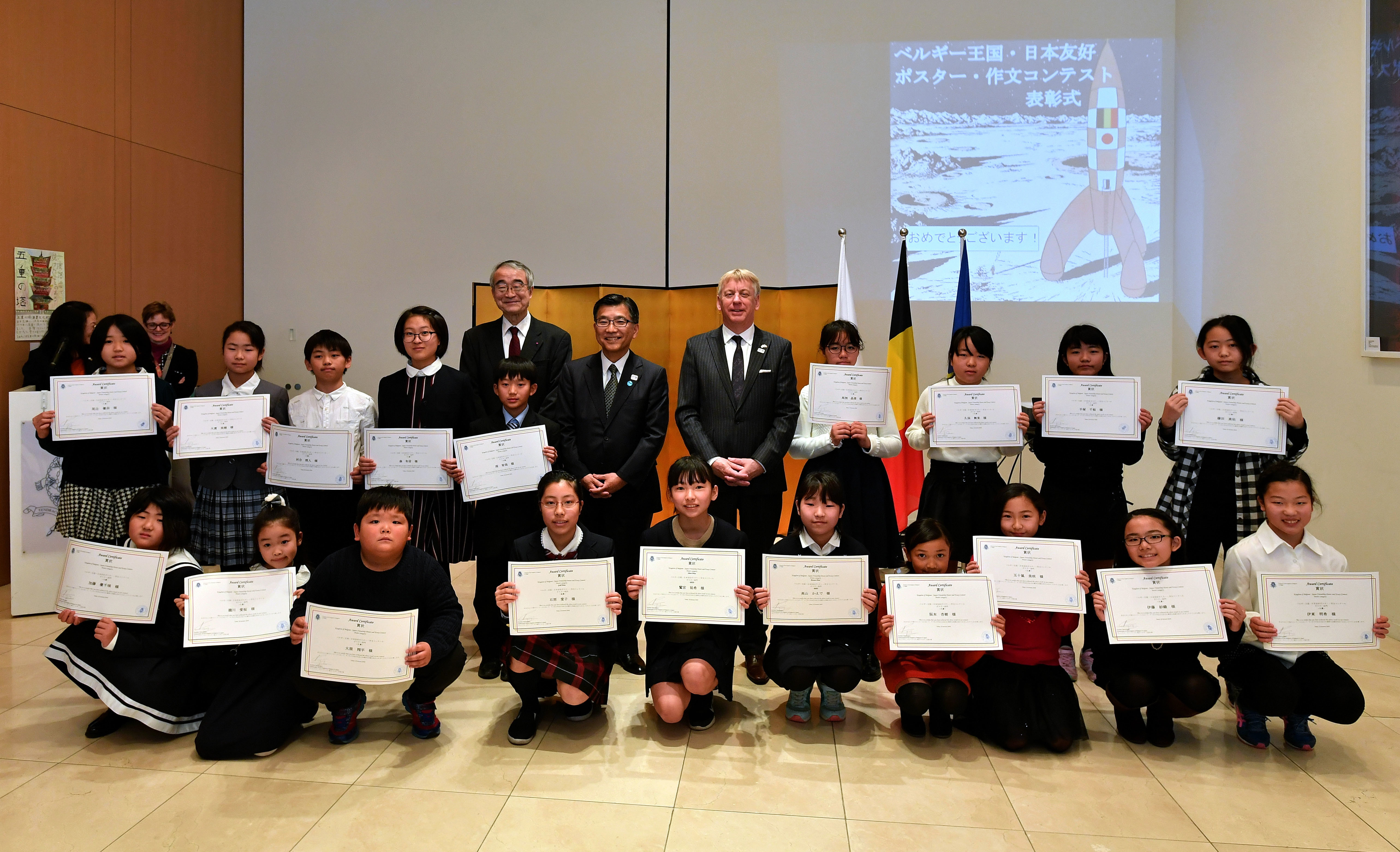 Students holding certificates pose for a photo during an awards ceremony for a poster and essay writing competition titled 