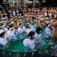 Men wearing loin cloths and women in robes pray as they bathe in ice-cold water during a ceremony to purify their souls and wish for good health in the new year at the Teppozu Inari Shrine in Tokyo on Sunday. | REUTERS