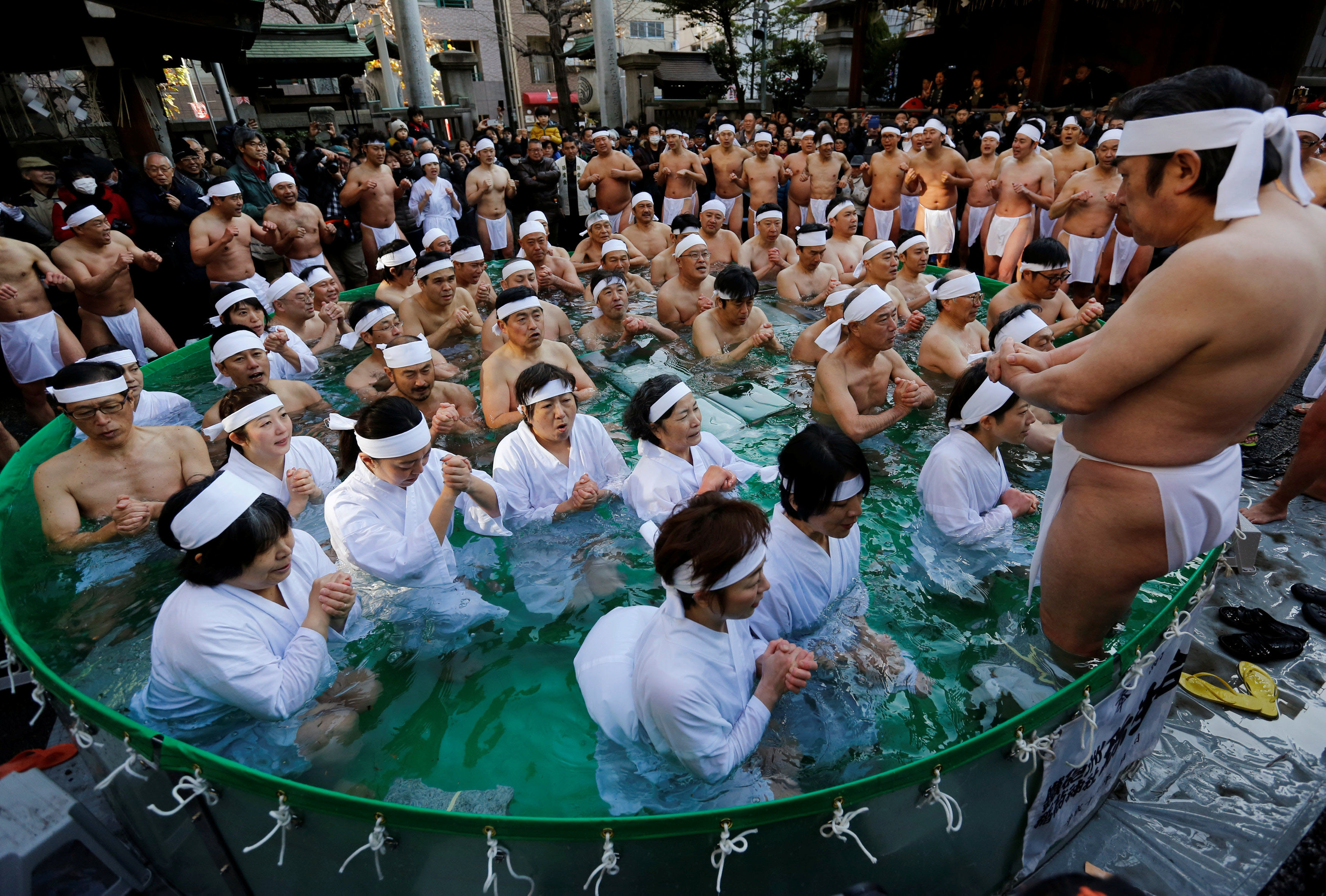 Men wearing loin cloths and women in robes pray as they bathe in ice-cold water during a ceremony to purify their souls and wish for good health in the new year at the Teppozu Inari Shrine in Tokyo on Sunday. | REUTERS