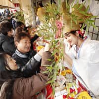 A shrine maiden at Imamiya Ebisu Shrine in Osaka\'s Naniwa Ward hands over decorated bamboo branches Wednesday as the annual Toka Ebisu festival begins. Many people visit the shrine, known for its \"divine help\" in achieving business prosperity, during the three-day festival. | KYODO