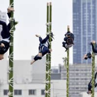 Firefighters from the Tokyo Fire Department perform traditional ladder stunts during the annual dezomeshiki New Year\'s event at Tokyo Big Sight in Koto Ward on Sunday. | KYODO