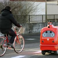 Japan Post Co. conducted a test run of a self-driving delivery robot that can also collect parcels in Namie, Fukushima Prefecture, on Thursday. The robot automatically stops when its sensor or camera detects a person in front of it. | KYODO
