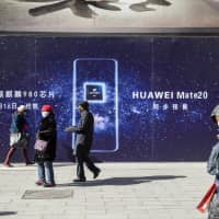 People walk past an advertisement for the Huawei Technologies Co. Mate 20 smartphone in Beijing on Friday. | BLOOMBERG