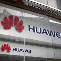 The logos of Huawei are displayed at its retail shop window reflecting the Ministry of Foreign Affairs office in Beijing in January. The head of Britain\'s cybersecurity agency says government oversight of Huawei has proven it can flag up security problems, suggesting he doesn\'t think the Chinese company needs to be banned from supplying mobile networks. | AP