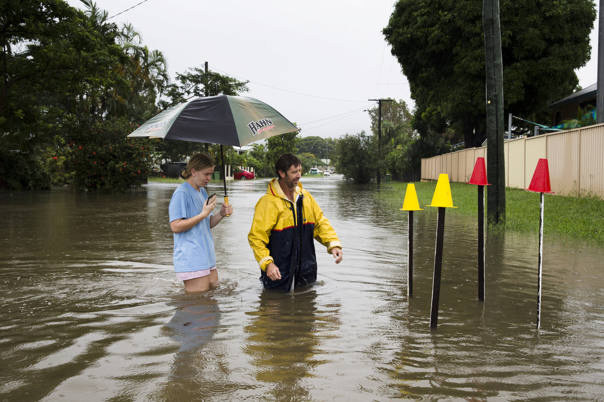 Residents of Townsville in northern Queensland stand in floodwater near pickets showing where a lid to a storm drain has been removed on Saturday. | REUTERS