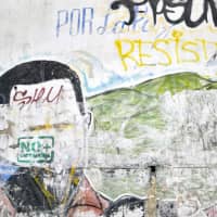 Graffiti reading \"No More Dictatorship\" is seen on a semi-erased image of the late Venezuelan President Hugo Chavez on a wall in the emblematic neighborhood of Petare in Caracas, Venezuela, on Jan. 18. | AFP-JIJI