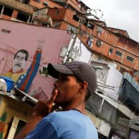 A local resident waits for a bus next to a graffiti of Venezuela\'s President Nicolas Maduro in the Jose Felix Ribas neighborhood of Caracas on Jan. 30. | REUTERS