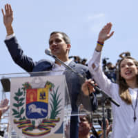 Juan Guaido, president of the National Assembly who swore himself in as the leader of Venezuela, and his wife Fabiana Rosales raise their hands during a pro-opposition protest in Caracas on Saturday. | BLOOMBERG