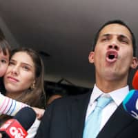 Venezuelan opposition leader and self-proclaimed interim president Juan Guaido talks to media next to his wife, Fabiana Rosales, who carrying their daughter outside their home after a meeting with supporters to present a government plan of the opposition in Caracas Thursday. | REUTERS