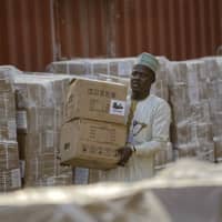 An electoral worker carries electoral materials past stacks of the papers to be used for recording results, at the offices of the Independent National Electoral Commission in Kano, northern Nigeria, Thursday. | AP