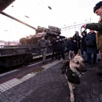A Russian serviceman with a sniffer dog stands near a train as people attend a mobile exhibition installed on freight cars and displaying military equipment, vehicles and weapons, which, according to Russia\'s Defense Ministry, were captured during its Syrian campaigns, upon its arrival at a railway station in Rostov-on Don, Russia, Wednesday. | REUTERS