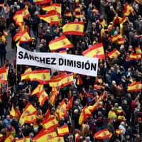 Right-wing protesters wave Spanish flags and hold a banner reading \"Sanchez, resign\" during a demonstration in Madrid against Spanish Prime Minister Pedro Sanchez on Sunday. | AFP-JIJI