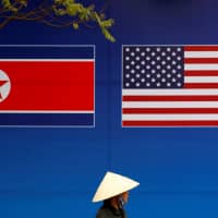 A person walks past a banner showing North Korean and U.S. flags ahead of the North Korea-U.S. summit in Hanoi, Vietnam. | REUTERS