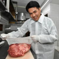 Mikio Atobe, chief executive of Meat Epoch Co., shows how to wrap a chunk of meat in an aging sheet &#8212; elastic netting lathered with spores to facilitate the dry aging of beef, fish and other types of animal flesh, on Jan. 18 in Tokyo. | YOSHIAKI MIURA