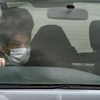 Yukinobu Tomita (seated at rear, wearing a hood) is taken to a police station in Hiroshima Prefecture on Wednesday after being arrested in Otsu, Shiga Prefecture, over a murder-robbery. | KYODO