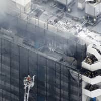 A firefighter on a fire truck ladder approaches a warehouse in Ota Ward, Tokyo, on Tuesday afternoon. The fire left three men dead and another man injured, and disrupted some flights at nearby Haneda airport. | KYODO
