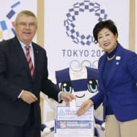 International Olympic Committee President Thomas Bach puts a mobile phone in a collection box for unwanted digital devices at the Tokyo Metropolitan Government building on Nov. 25 while posing with Tokyo Gov. Yuriko Koike. | KYODO