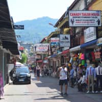 Tourists walk down a street in Patong featuring a number of tailoring shops. | JOEL TANSEY