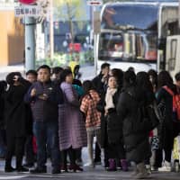 Chinese tourists wait near a tour bus in the Ginza district in Tokyo. As countries from Palau to South Korea have learned the hard way, the Chinese government isn\'t afraid to divert its tourists and their thick pocketbooks whenever it wants to make a political point. | BLOOMBERG