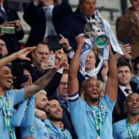Vincent Kompany lifts the trophy as Manchester City celebrates winning the League Cup on Sunday in London. | REUTERS
