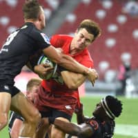 The Sunwolves\' Gerhard van den Heever is tackled by Sharks players during their game on Saturday in Singapore. | AFP-JIJI
