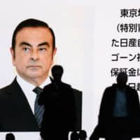 Pedestrians walk past a screen displaying a news broadcast on former Nissan Motor Co. chief Carlos Ghosn in Tokyo on Tuesday. | BLOOMBERG