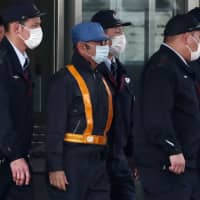 Ousted Nissan chief Carlos Ghosn, wearing a blue cap, is escorted out of the Tokyo Detention House following his release on bail in Tokyo on Wednesday. | AFP-JIJI