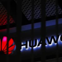A logo of Huawei retail shop is seen through a handrail inside a commercial office building in Beijing Friday. Chinese tech giant Huawei\'s tensions with Washington, which accuses the telecom equipment maker of being a security risk, stretch across four continents from courtrooms to corporate boardrooms to Canadian canola farms. | AP