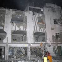 Somalis walk near a destroyed building after a car bomb in Mogadishu Thursday. At least four people were killed in a powerful explosion late Thursday, police said, in an attack that Islamic extremists said was an attempt to bomb a hotel. | AP