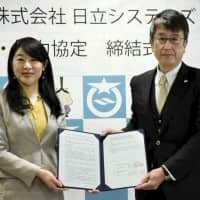 Otsu Mayor Naomi Koshi (left) and Hitachi Systems Ltd. executive Koji Higashi show off a signed agreement to the media Friday over using Hitachi\'s artificial intelligence expertise to help teachers detect signs of serious bullying in schools. | KYODO