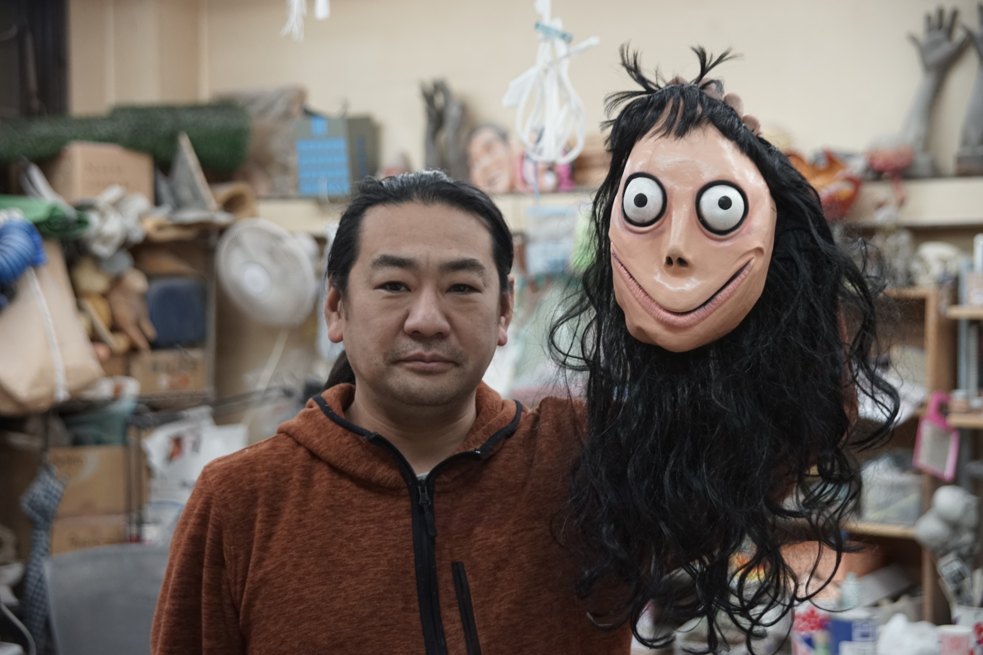 Artist Keisuke Aiso, creator of the goggle-eyed creature that was later dubbed Momo, holds up an unauthorized replica mask of the monster that a friend brought back as a souvenir from Mexico's Day of the Dead festivities, at his two-story studio on the outskirts of Tokyo on Monday. | RYUSEI TAKAHASHI