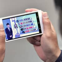 A man watches an NHK program on his cellphone. The top court says owners of cellphones with television functions must pay subscription fees to the public broadcaster. | KYODO