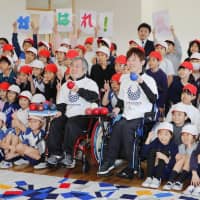 Takayuki Hirose (left) and Hidetaka Sugimura who competed on Japan\'s silver medal-winning mixed boccia team at the 2016 Paralympics, pose with students at Ariake Nishi Gakuen, an elementary and middle school, in Tokyo on Friday. | KYODO